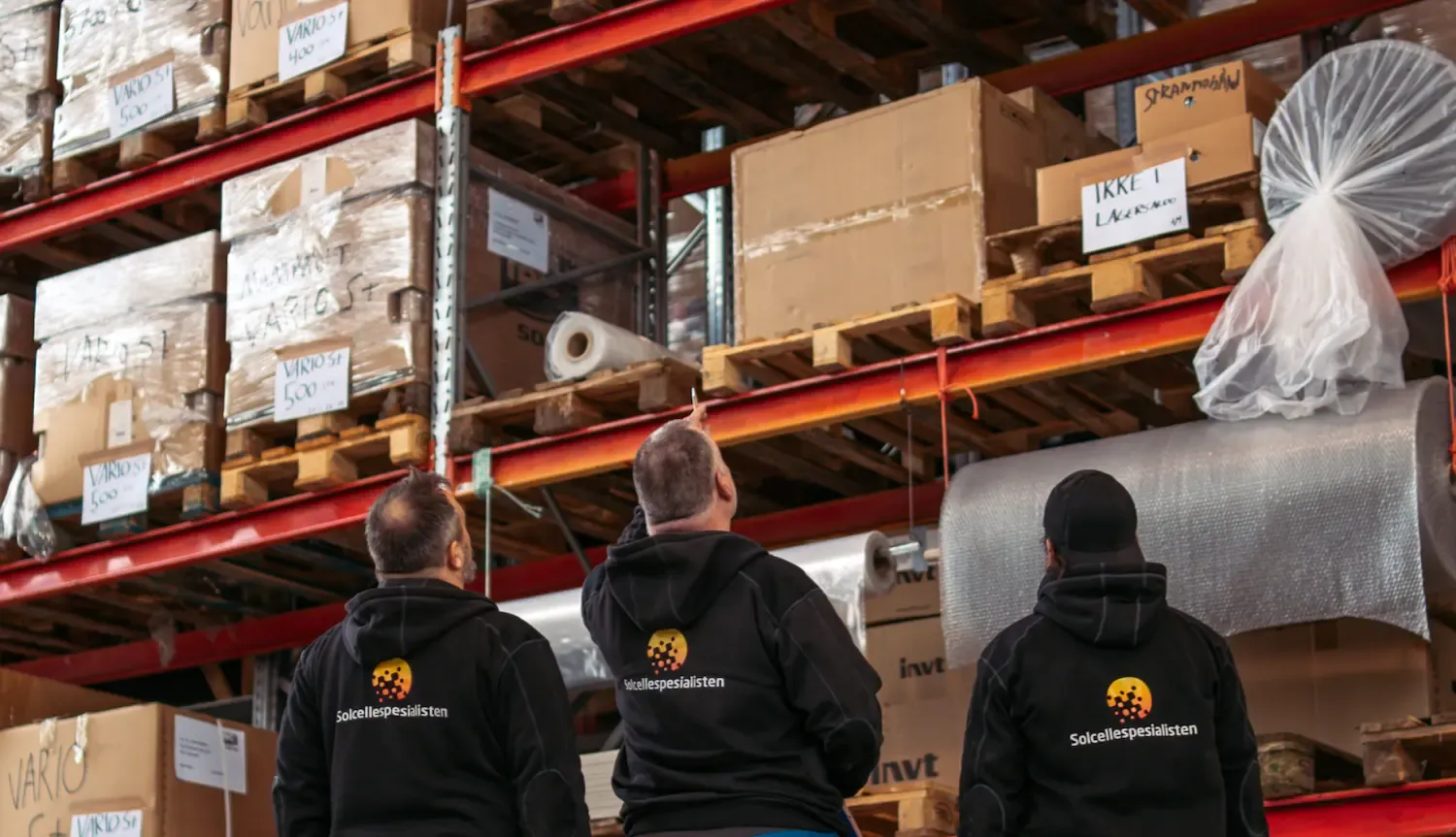 Tre ansatte i Solcellespesialisten-gensere foran høye pallereoler på sentrallageret