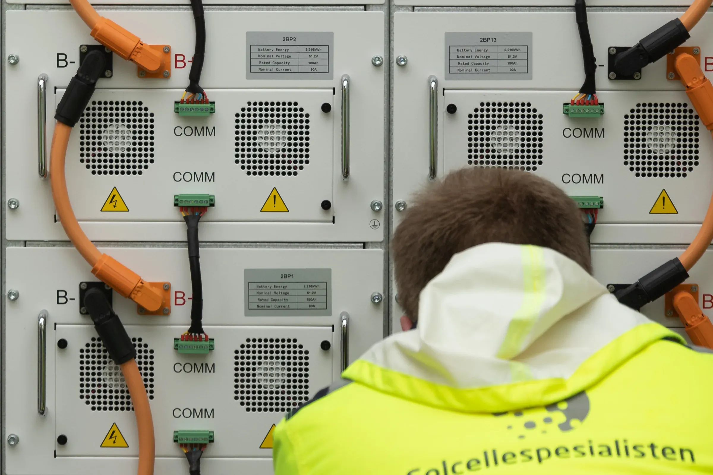 Montør i Solcellespesialisten-jakke arbeider ved batterimoduler i et batterirack