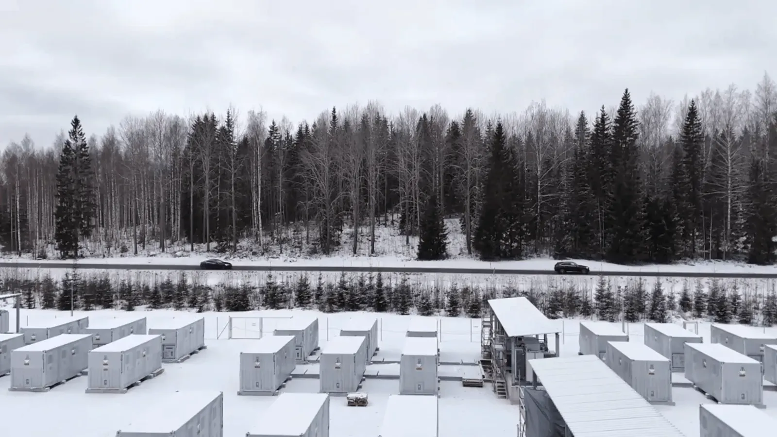 Containerbaserte batterianlegg på rekke i et snødekt landskap med granskog