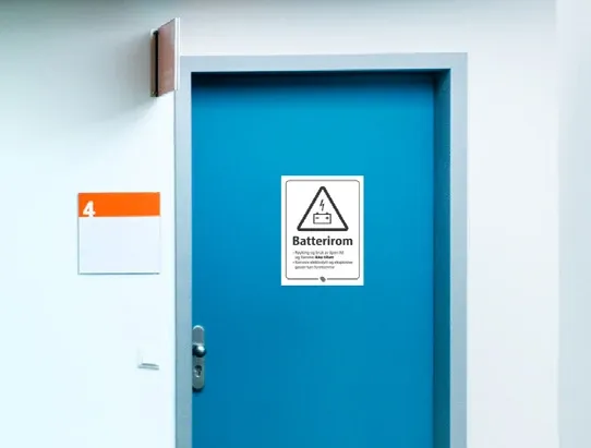 Blå dør i en korridor med et hvitt skilt merket «Batterirom» med varseltrekant og batterisymbol